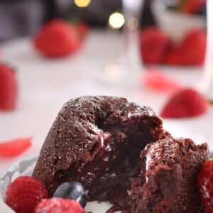 Gluten-free chocolate molten lava cake split open with it's gooey center showing surrounded by fresh berries and champagne glasses.