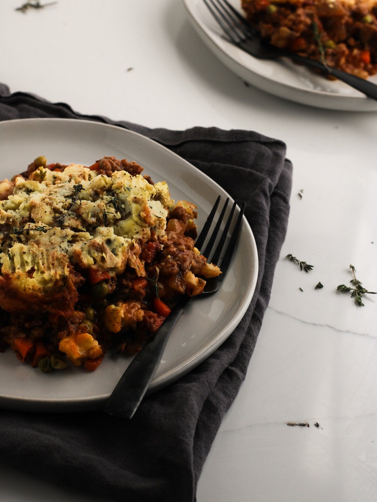 Shepherd's pie on a plate laying over a grey table linen ready to be enjoyed.